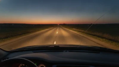 Route de campagne au crepuscule vue depuis l'interieur d'une voiture, phares allumes